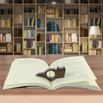 Bague de lecture Le Chat Lecteur en bois posée sur un livre ouvert, devant une bibliothèque