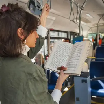 Lectrice debout dans le bus, livre tenu d'une main grâce à la bague de lecture en bois sur son pouce