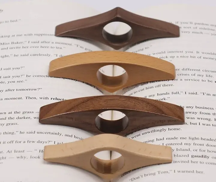 Les quatre teintes de la bague de lecture en bois posées sur un livre ouvert : noyer, chêne doré, acajou, érable naturel