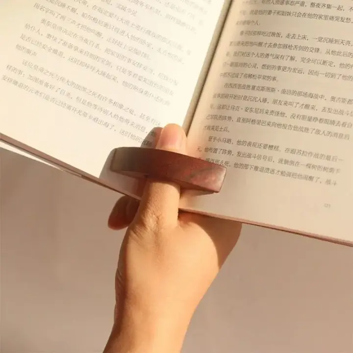 Bague de lecture en bois glissée sur le pouce, qui maintient les deux pages d'un livre ouvertes